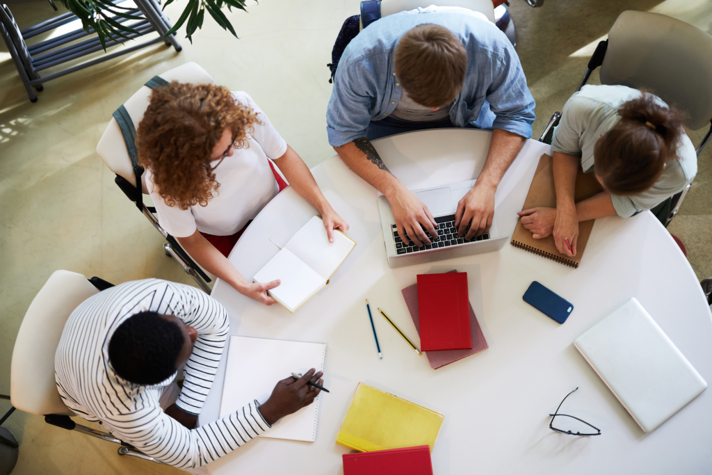 a group of people sitting around a table with laptops